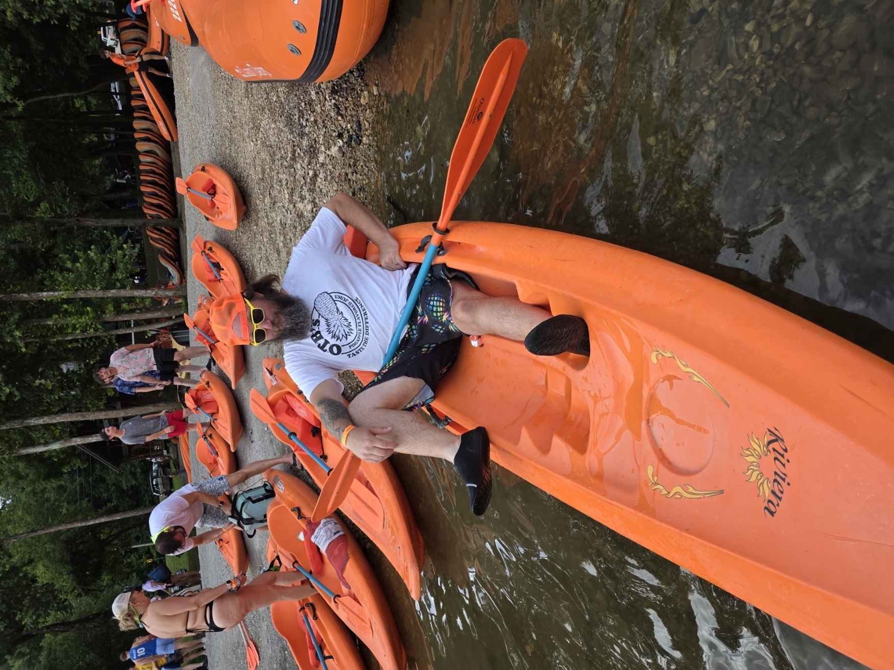 OTB guest relaxing in a kayak at the riverbank in an OTB shirt
